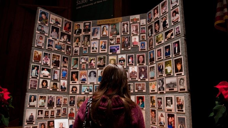 A woman looks at a wall of photos of people...