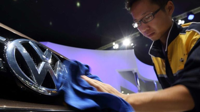 A worker wipes the Volkswagen logo on a vehicle displayed...