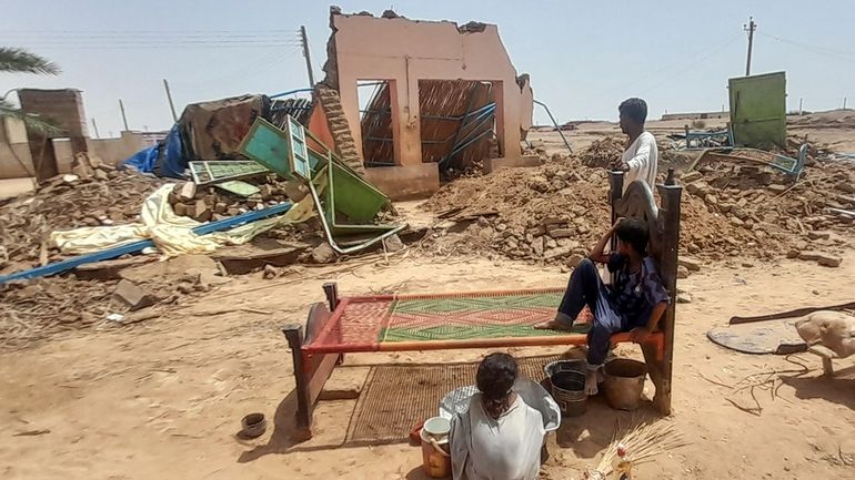 People sit in front of their home damaged by floods...