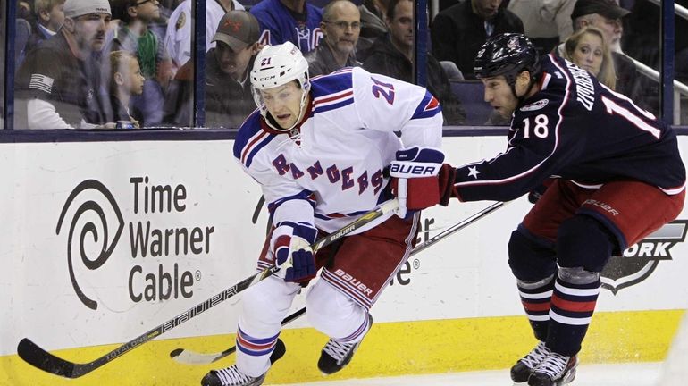 Derek Stepan, left, carries the puck behind the net as...