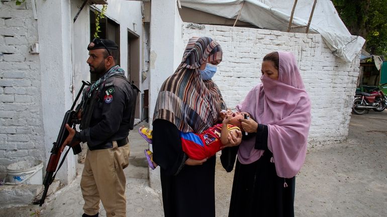 A police officer stands guard as a health worker, right,...