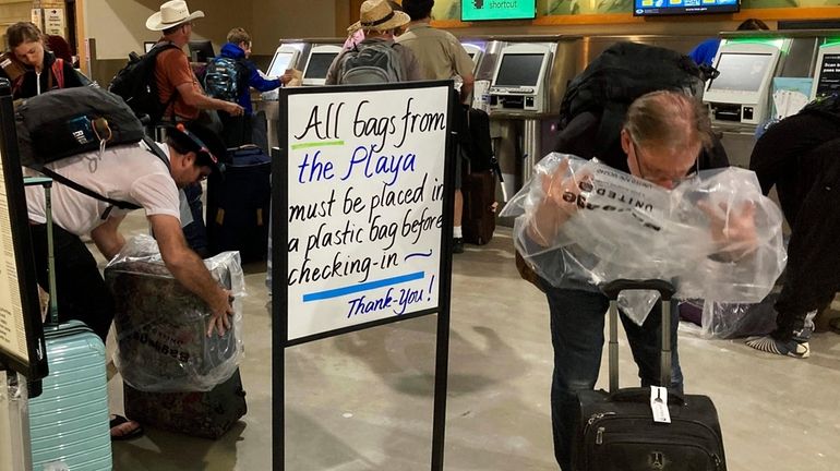 Burning Man attendees place plastic bags over the baggage at...