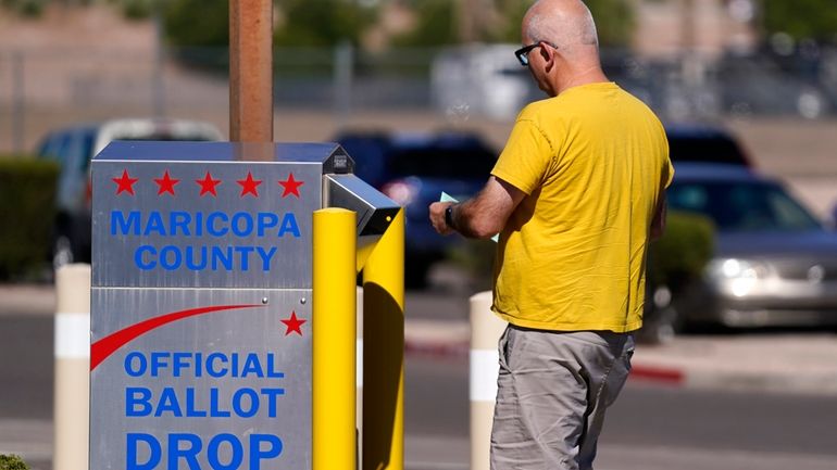 A voter places a ballot in an election voting drop...