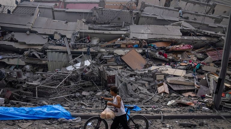 A Palestinian child walks with a bicycle by the rubble...