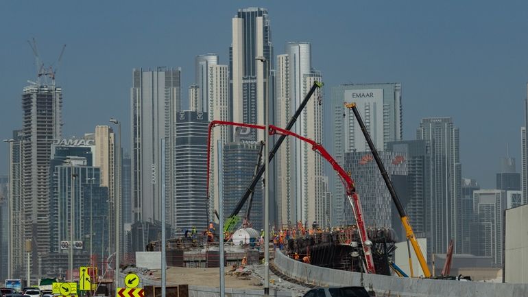 Laborers work at a construction site with skyscrapers towering in...