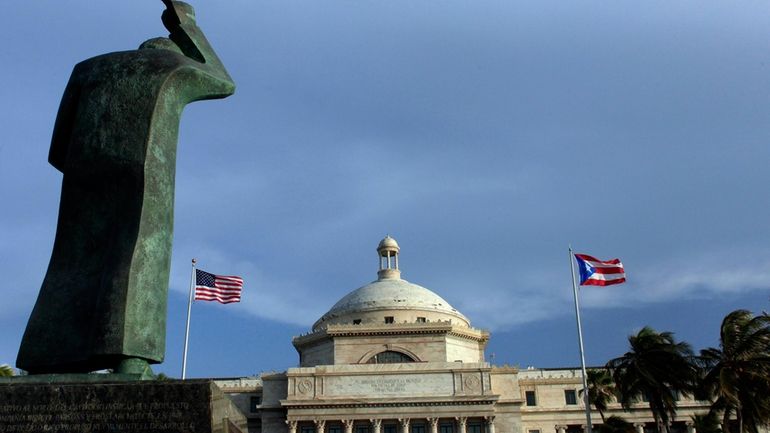 A bronze statue of San Juan Bautista stands in front...