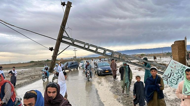 People pass by a damaged electric pole caused by flooding...