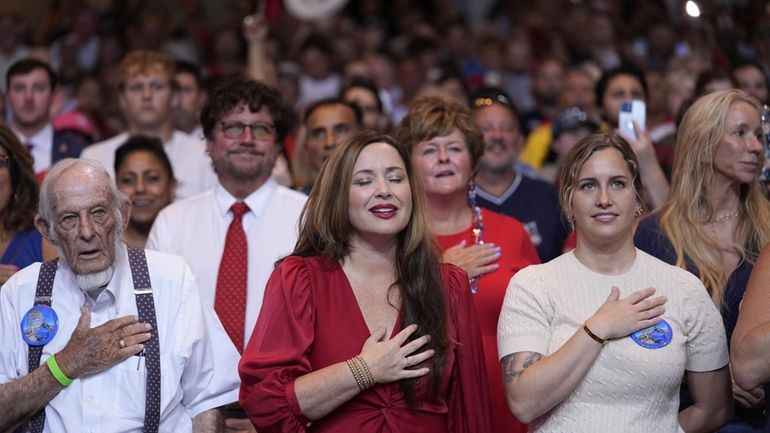 Audience members stand to say the Pledge of Allegiance before...