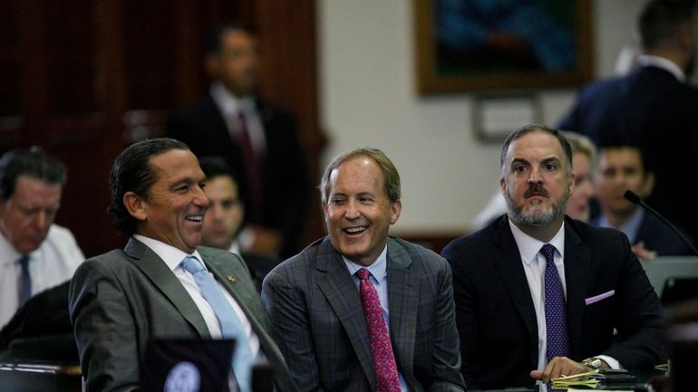 Texas Attorney General Ken Paxton, center, sits between defense attorneys...