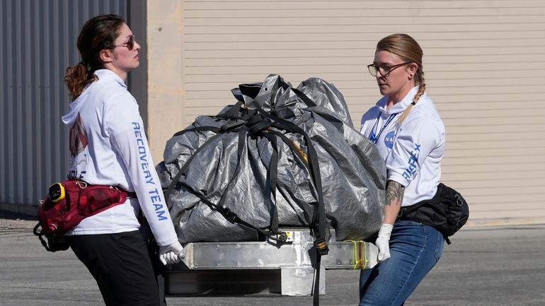 Recovery team members carry a capsule containing NASA's first asteroid...