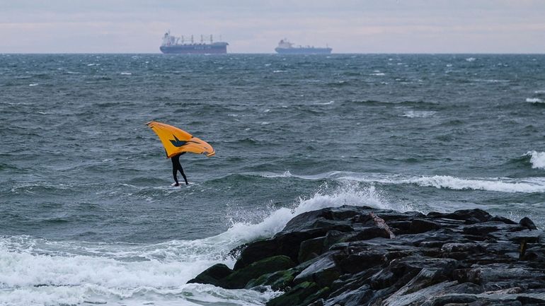 A lone wind surfer rides the waves on a cold,...