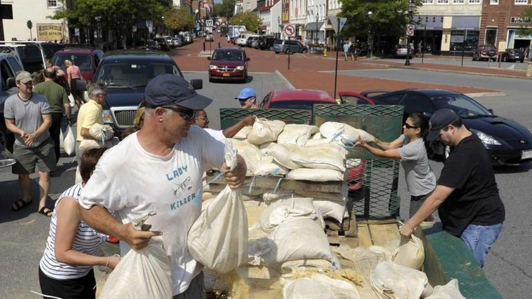 People take sandbags off a truck as residents prepare for...