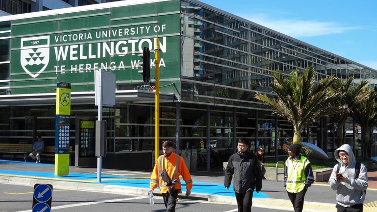 People walk past the name of Victoria University of Wellington,...