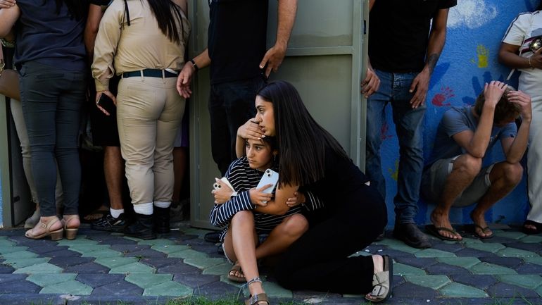 Israelis take cover next to a shelter as a siren...