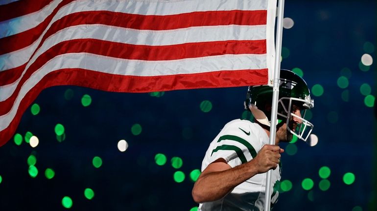 Jets quarterback Aaron Rodgers carries an American flag onto the...