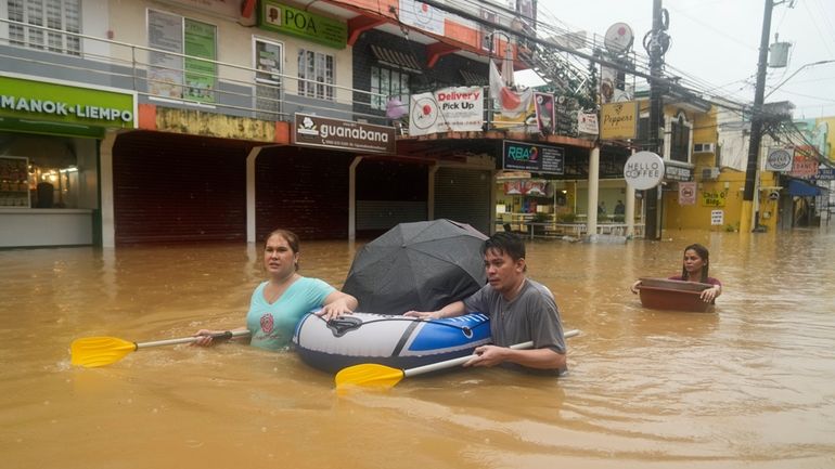 Residents use rubber paddles from a toy boat as they...