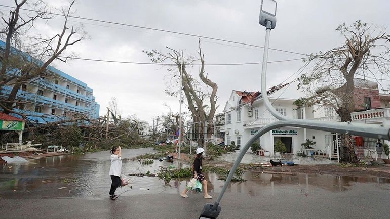 People walk past broken light post after typhoon Yagi hit...