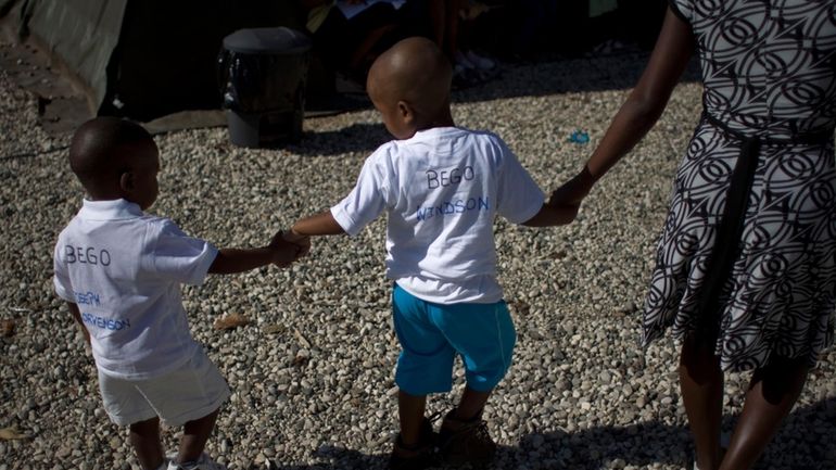 Haitian children walk hand in hand as they await the...