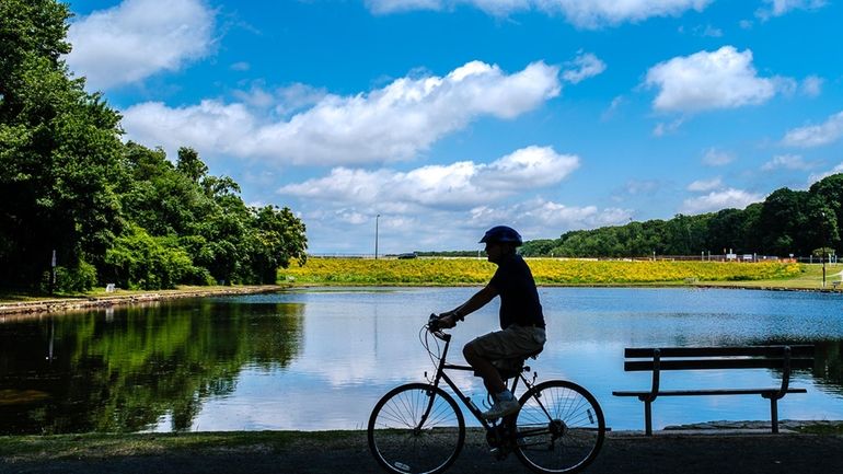 A cyclist rides on a shaded path along the shore...