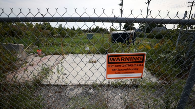 A sign warning of beryllium hangs on a fence at...