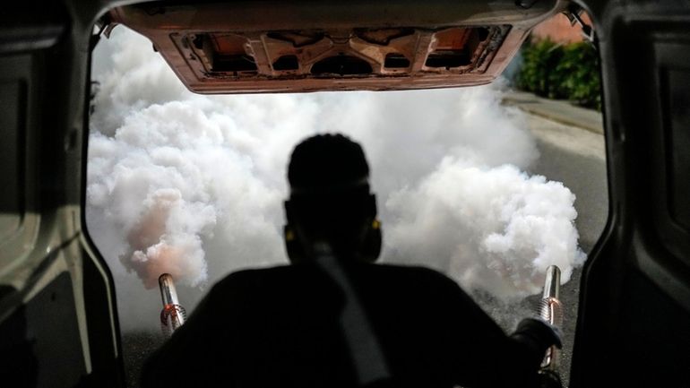 A worker fumigates a neighborhood against dengue-promoting mosquitoes, in Caracas,...