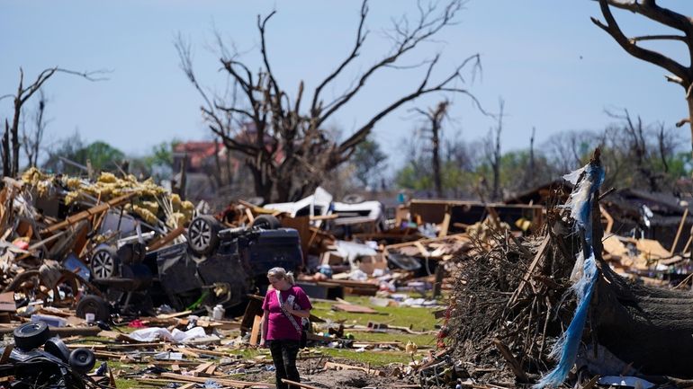 A woman walks near an uprooted tree, a flipped vehicle...