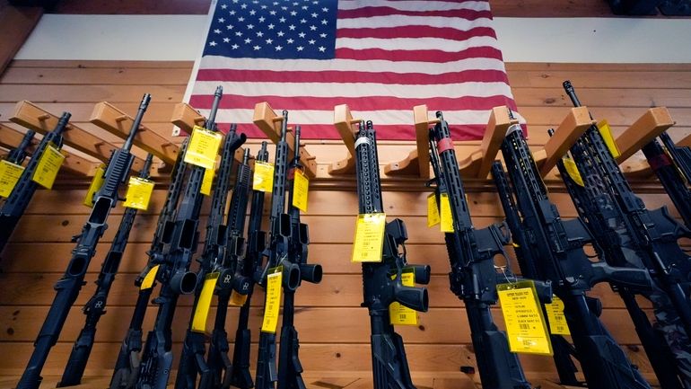 A variety of AR-15-style rifles are displayed under an American...