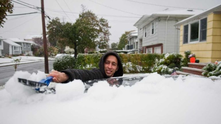 Michael Neiss uncovers his car with snow in front of...