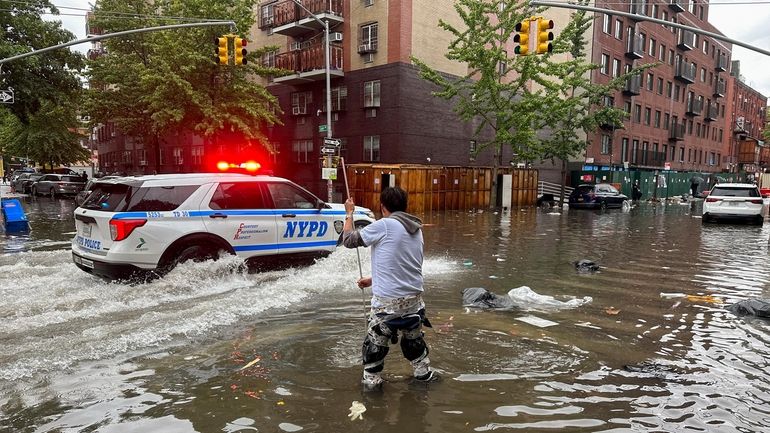 A man works to clear a drain in flood waters,...