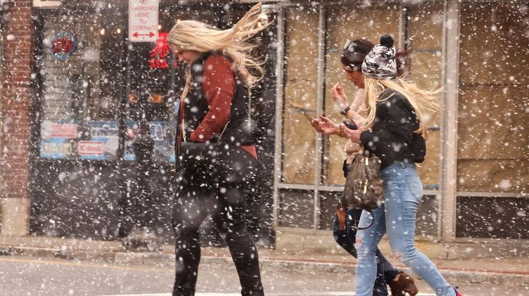 People shield themselves from the snow while walking down Main...