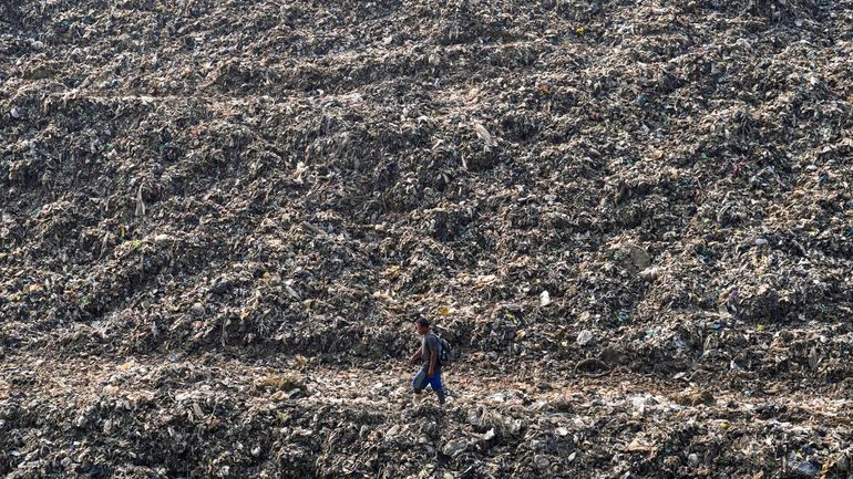 A wastepicker walks past on a pile of garbage at...