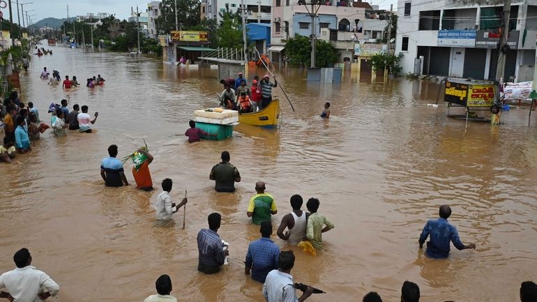 People wade through a flooded road after heavy rains in...