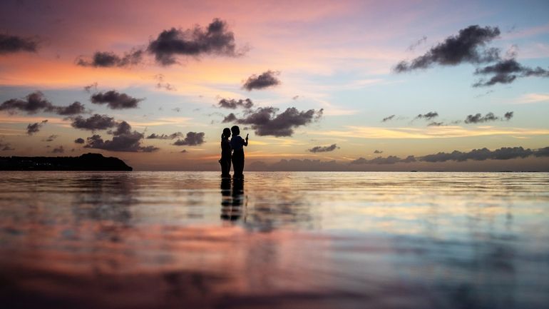 Tourists watch the sun set along a popular beach in...