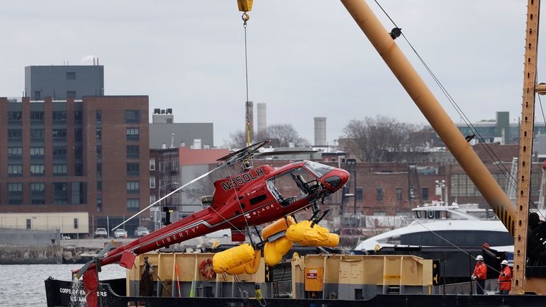 A helicopter is hoisted by crane from the East River...