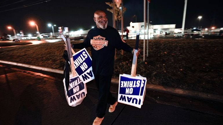 United Auto Workers member Marcel Edwards carries On Strike signs...