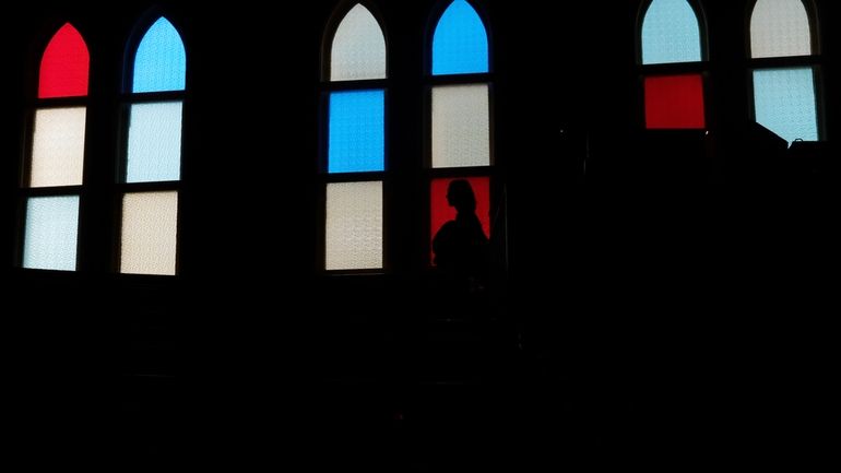 A woman is silhouetted against the stained-glass windows at the...