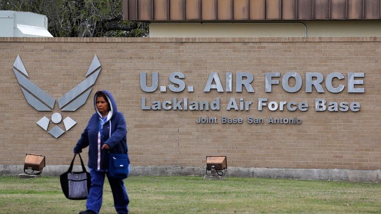 A pedestrian passes the main gate at Lackland Air Force...