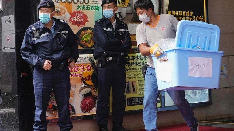 A worker carrying some containers walks past police officers during...