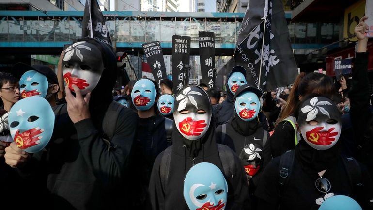 Pro-democracy protesters wear masks depicting the hand with Chinese Communist...