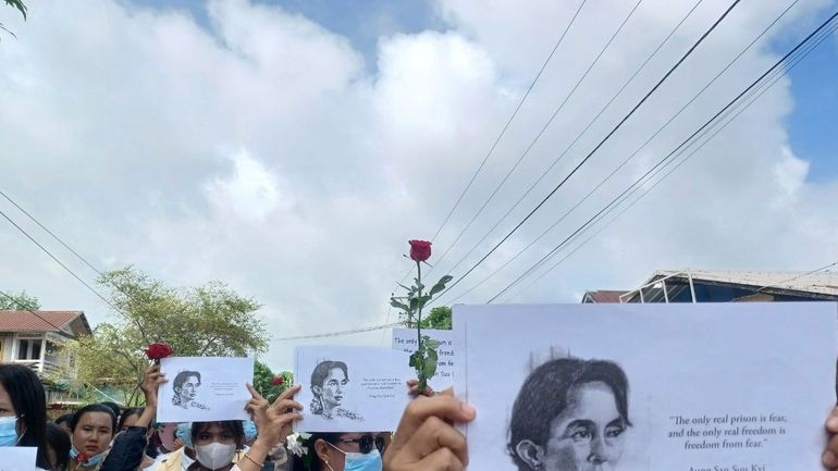 Demonstrators hold papers printed with Aung San Suu Kyi’s famous...