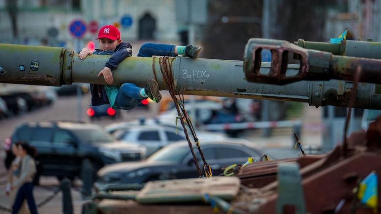 A boy holds on to the barrel of a tank,...