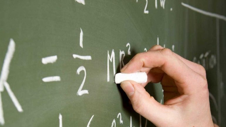 A student writes out a math problem on a chalkboard.