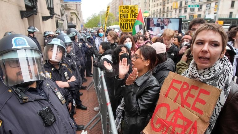 Police in Riot gear stand guard as demonstrators chant slogans...