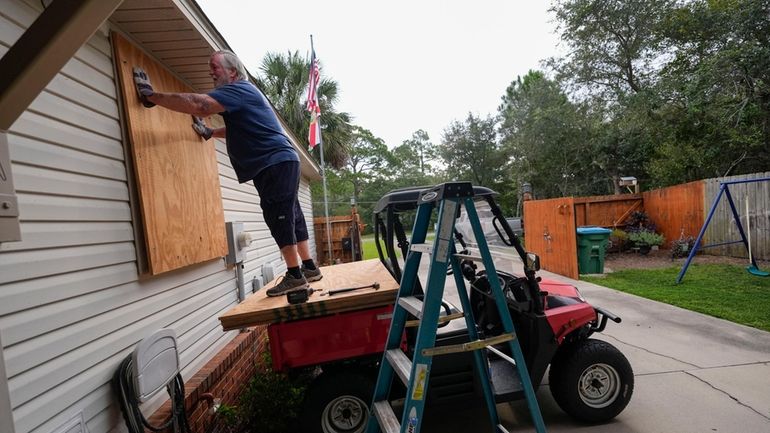 Dave McCurley boards up the windows to his home in...