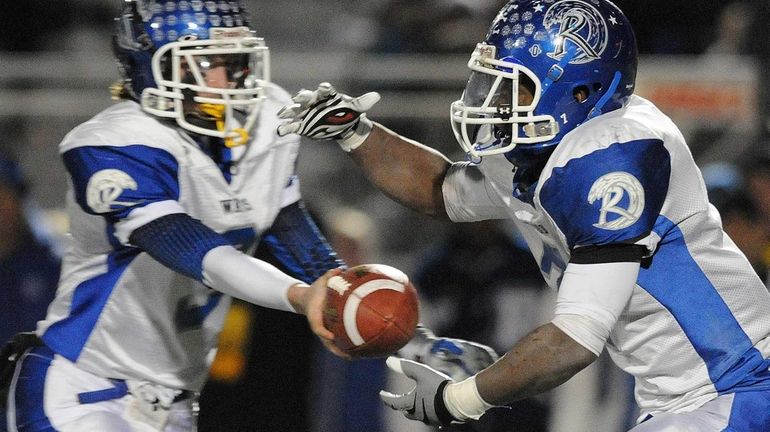 Riverhead's Ryun Moore (right) takes a handoff from quarterback Cody...