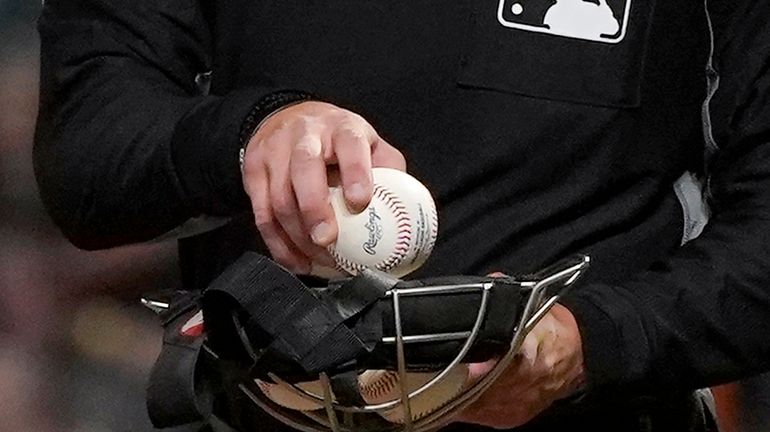 An umpire puts a ball into his face mask during...