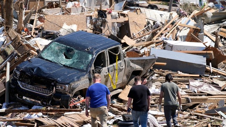 Local residents walk among the debris from tornado damaged homes,...