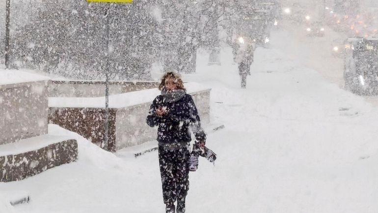 A man walks down a street during heavy snowfall in...