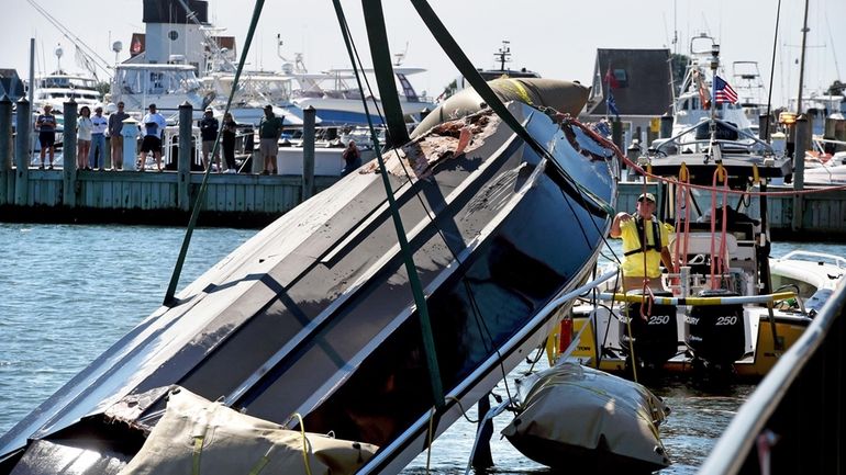 A capsized boat with a damaged hull is lifted out...