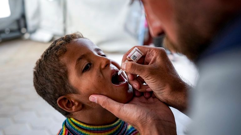 A health worker administers a polio vaccine to a child...